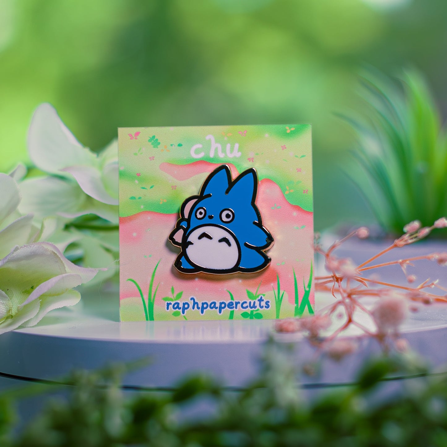 Card with a cartoon character and 'chu' text on a table with flowers and plants.